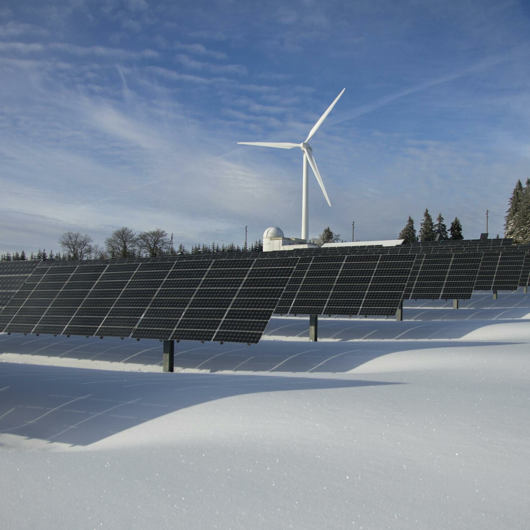 Solar panels and wind turbine in a snowy landscape, showcasing renewable energy sources.